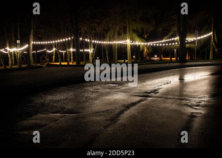 Park oder Garten mit warmen Glühbirnen, Straßenlampen am Abend oder in der Nacht, dekorative Beleuchtung, Feier, gemütlichen Hintergrund, nasse Straße oder Straße Stockfoto