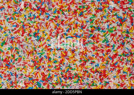 Regenbogen-Streuseln, Hintergrund und Oberfläche. Stangenförmige bunte Zuckerstreuseln. Kleine Bonbons in verschiedenen Farben, als Dekoration oder Topping verwendet. Stockfoto