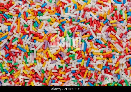 Regenbogen-Streuseln, Hintergrund und Oberfläche. Stangenförmige bunte Zuckerstreuseln. Kleine Bonbons in verschiedenen Farben, als Dekoration oder Topping verwendet. Stockfoto