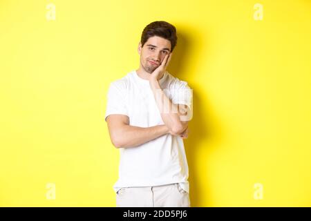 Gelangweilter und unamüsiert Mann, der mit Gleichgültigkeit schaut, in weißen Kleidern über gelbem Hintergrund stehend Stockfoto