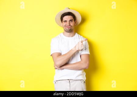 Skeptischer männlicher Tourist, der sich beschwert, mit dem Finger auf etwas Schlechtes oder Lahmes zeigt, unamüsiert vor gelbem Hintergrund steht Stockfoto