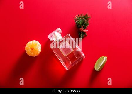 Eine Flasche Parfüm im Dekor von Christbaumzweigen, Mandarine und Limette auf rotem Hintergrund Stockfoto