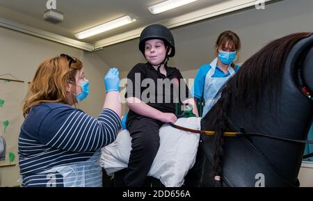 East Lothian, Scotland, UK, NHS Lothian & Muirfield Riding Therapy feiert 10 Jahre Hippotherapie: Physiotherapeutin Heather Falconer ist Vorreiter des Children’s Therapeutic Riding Service, der Kindern, Jugendlichen und Erwachsenen mit Behinderungen kostenloses therapeutisches Reiten bietet. Der Service war der erste in Schottland für Kinder mit Beweglichkeit, Balance, Muskeltonus und Koordinationsproblemen. Oreo, ein mechanisches Pferd, ermöglicht es Jugendlichen, Spaß Physiotherapie haben. Louis MacDiarmid, 10 Jahre alt, reitet auf dem mechanischen Pferd von Racewood Stockfoto