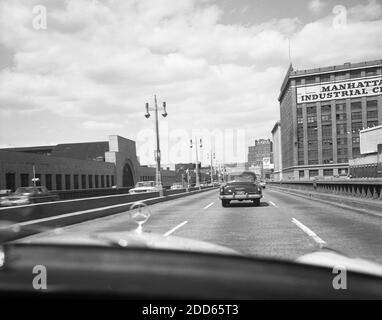 Historische Automobile aus den 1960er Jahren auf einer kopfsteingepflasterten Brücke, die das große Gebäude des Manhattan Industrial Center in der West 15th Street und 10th Avenue in New York, USA, verbindet. Das Gebiet des Industriezentrums war aufgrund seiner historischen Geschäftstätigkeit als Fleischpackungsviertel bekannt. Stockfoto