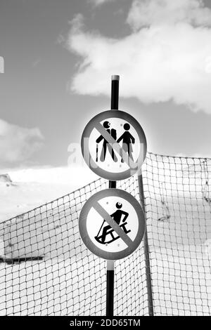 Verschneite Skipiste, Zaun und zwei Verkehrsverbotszeichen auf Skigebiet an sonnigen Wintertag. Schwarzweißbild. Stockfoto