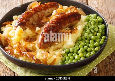 Gebratene Würstchen mit Kartoffelpüree, Zwiebelsoße und grünen Erbsen in einem Teller auf dem Tisch. Horizontal Stockfoto