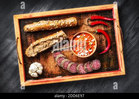 Rustikales Holztablett mit einfachen Balkan-Lebensmitteln - Ajvar Aufstrich, Brot, Fleisch, Knoblauch und Chili (selektiver Fokus) Stockfoto