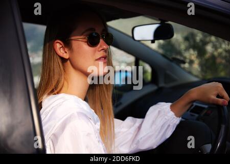 Junge Frau trägt Sonnenbrille hinter dem Lenkrad auf der Straße Reise Urlaub durch offene Tür des Mietwagens Stockfoto