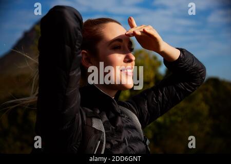 Aktive junge Frau trägt Rucksack auf Wanderung in Landschaft Abschirmung Ihre Augen von der Sonne Stockfoto