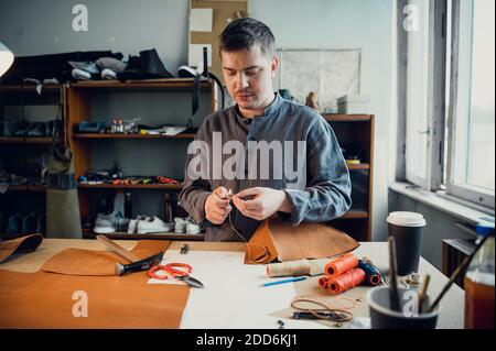 Porträt eines professionellen Schuhmachers im Inneren einer Schuhmacherwerkstatt, die eine Tasche aus echtem Leder macht. Stockfoto