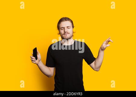 Langhaariger kaukasischer Mann mit Bart und schwarzem T-Shirt hören Zum Musieren über Telefon und Kopfhörer Stockfoto