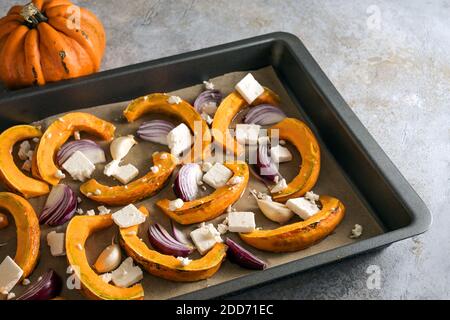 Backblech mit rohen Kürbisscheiben, roten Zwiebeln und Feta-Käse bereit für den Ofen, Kochen mit Herbstgemüse an Thanksgiving und Halloween, sele Stockfoto