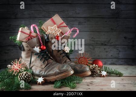 Alte Wanderschuhe gefüllt mit Süßigkeiten, Geschenken und Weihnachtsdekoration am Nikolaus-Tag, oder deutscher Nikolaus-Tag, am 6. Dezember ist es Tradition zu pu Stockfoto