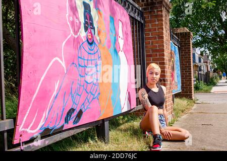 Eine junge Künstlerin sitzt stolz vor ihr Wandgemälde auf der Straße Stockfoto