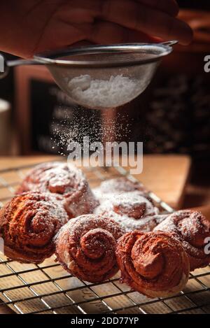 Nahaufnahme Koch streuen Puderzucker über den Zimt Rollen Stockfoto