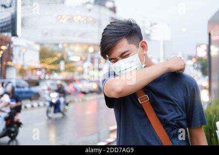 Nahaufnahme junger Mann mit schützender Gesichtsmaske hustet in seinem Ellbogen. Niesen korrigieren. Konzept der Stop-Ausbreitung des Virus. Stockfoto
