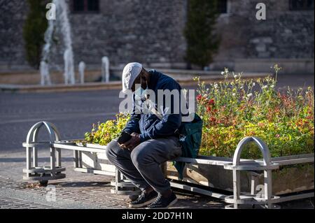 terni, italien november 11 2020: Schwarzer Mann mit medizinischer Maske sitzt auf Ein Pflanzgefäß Stockfoto