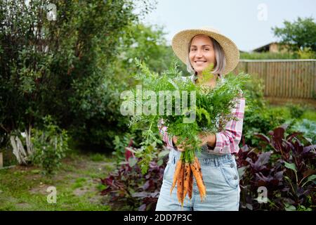 Nettes Mädchen trägt Hut pflücken Karotten in einem Garten. Frische Karotten aus dem Garten gepflückt. Ernte. Landwirtschaft Stockfoto