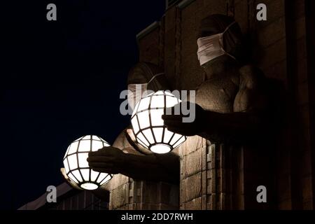 Zwei Statuen, die kugelförmige Lampen halten und Gesichtsmasken tragen Der Eingang zum Hauptbahnhof von Helsinki Stockfoto