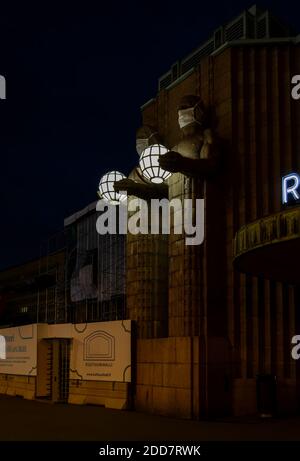 Zwei Statuen, die kugelförmige Lampen halten und Gesichtsmasken tragen Der Eingang zum Hauptbahnhof von Helsinki Stockfoto