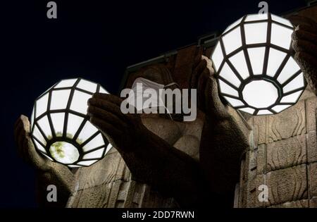 Zwei Statuen, die kugelförmige Lampen halten und Gesichtsmasken tragen Der Eingang zum Hauptbahnhof von Helsinki Stockfoto