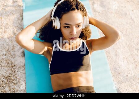 Athletische junge afroamerikanische Frau, die Musik auf Kopfhörer hören, tun Bauchübungen, um die wichtigsten Bauchmuskeln zu stärken, liegen auf einem Stockfoto