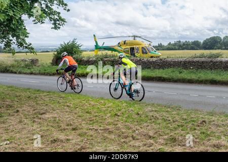 2 Radfahrer auf eine Fahrt auf einem ruhigen Land Road Passing der Wiltshire Air Ambulance Hubschrauber landete in einem Feld, während Sanitäter einen Unfall in besuchen Stockfoto