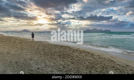 Mann läuft auf einem einsamen Strand bei Sonnenuntergang an einem bewölkten Tag, Playa de Muro, Palma de Mallorca, Balearen, Spanien, Panorama-Format Stockfoto