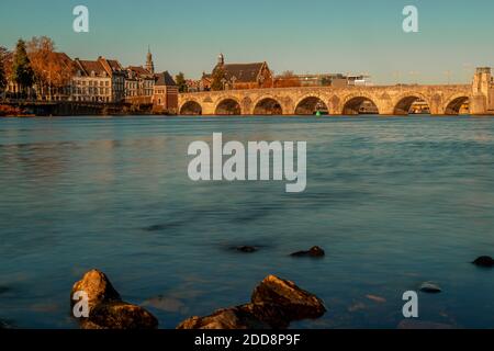 Blick über das Wasser mit der historischen Skyline von Maastricht mit der alten Brücke, die zwei Teile der Stadt über die Maas verbindet. Stockfoto