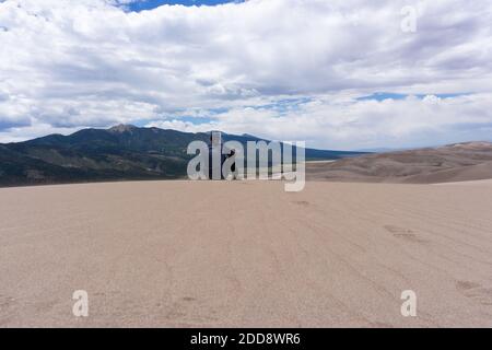 Mann sitzt vor den Bergen in Great Sand Dunes Nationalpark Stockfoto