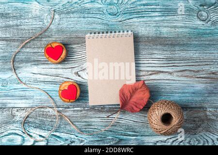 Notizblock und zwei rote Herzen auf einem grau-blauen Hintergrund aus Holz. Stockfoto