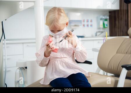 Ein süßes kleines Mädchen, das mit einem künstlichen Kiefer und medizinischen Instrumenten in einer Zahnarztpraxis spielt. Stockfoto