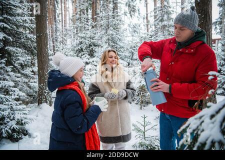 Eine aktive Familie mit zwei Kindern spaziert durch ihr Anwesen im Winterschneewald außerhalb der Stadt und trinkt heißen Kaffee aus einer Thermoskanne, um sich warm zu halten Stockfoto