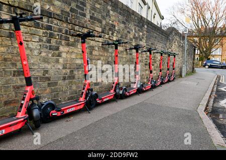 Vermietung von Motorroller von VOI, aufgereiht entlang einer Ziegelmauer im Stadtzentrum von cambridge, Roller werden über Telefon-App gemietet. Stockfoto