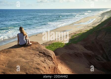 Frau, die auf Felsformationen sitzt und auf das Meer blickt Stockfoto