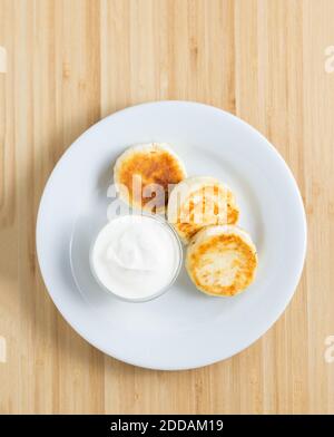 Hüttenkäse Pfannkuchen mit saurer Sahne auf dem Holzhintergrund Stockfoto