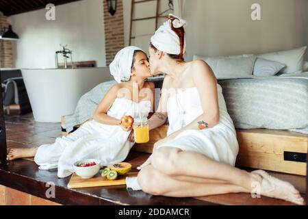 Mutter und Tochter im Handtuch küssen, während im Schlafzimmer sitzen Zu Hause Stockfoto