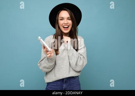 Bild von einer glücklichen jungen schönen Frau posiert isoliert über Blauer Wandhintergrund mit Mobiltelefon Stockfoto