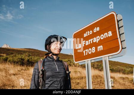 Lächelnde Frau mit mittlerem Erwachsenen, die Radhelm trägt, steht an der Tafel im Somiedo Naturpark, Spanien Stockfoto