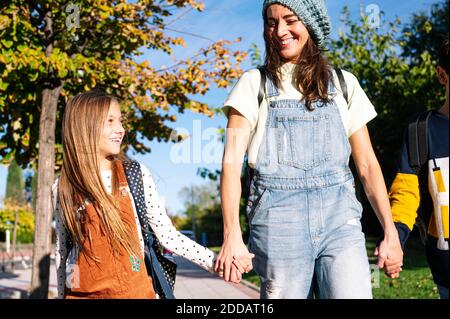 Lächelnde Mutter, Tochter und Sohn halten sich die Hände, die am sonnigen Tag im öffentlichen Park spazieren gehen Stockfoto