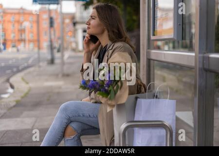 Junge Frau im Gespräch auf Smartphone mit Einkaufstaschen während Sitzen in der Stadt Stockfoto