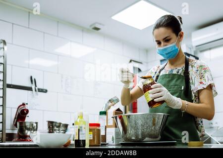 Junge Bäckerin trägt Schutzmaske beim Plätzchen machen in Bäckerei während Coronavirus Stockfoto