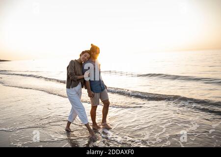Junges Paar, das während des Sonnenuntergangs am Strand entlang läuft Stockfoto