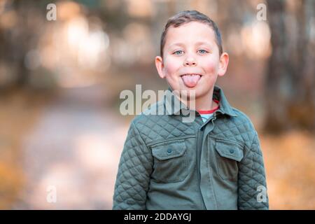 Junge, der im Herbst im Park steht und die Zunge herausstreckt Stockfoto