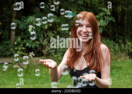 Glückliche Frau spielt mit Seifenblasen im Hinterhof Stockfoto