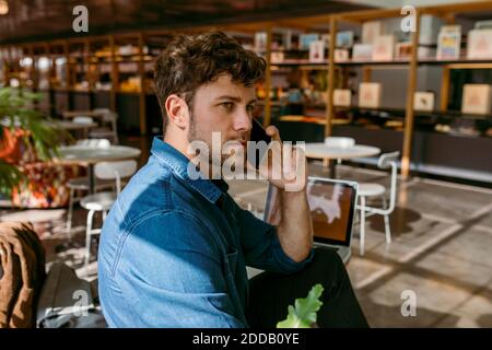 Serious junge Geschäftsmann wegschauen Gespräch auf Smartphone in Café Stockfoto