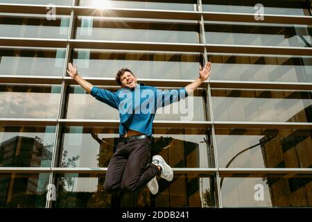 Unbeschwerter junger Geschäftsmann, der gegen ein modernes Bürogebäude springt Stockfoto