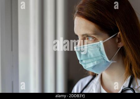 Nachdenkliche junge Ärztin mit Gesichtsmaske während COVID-19 Stockfoto