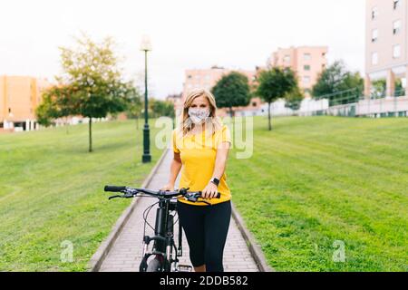 Frau trägt eine schützende Gesichtsmaske, die mit dem Fahrrad auf dem Fußweg steht In der Stadt während der COVID-19 Stockfoto