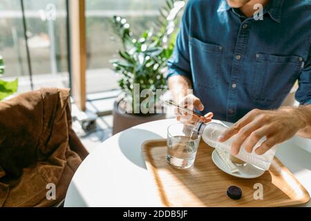 Junger Geschäftsmann mit Smartphone, während Wasser in Glas gießen Am Tisch im Café Stockfoto